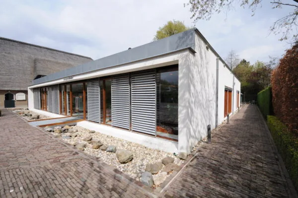 Modern laagbouwgebouw aan de Charloisse Lagedijk met grote ramen en horizontale zonwering, omringd door een bestrate wandelweg en siergrind.